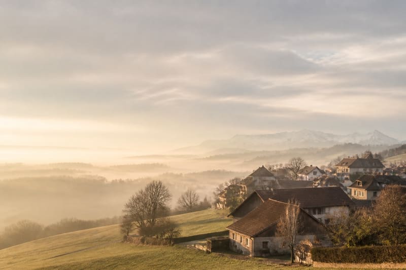 Schweizer Dorf in einer hügeligen Landschaft, im Dunst eines goldenen Morgens